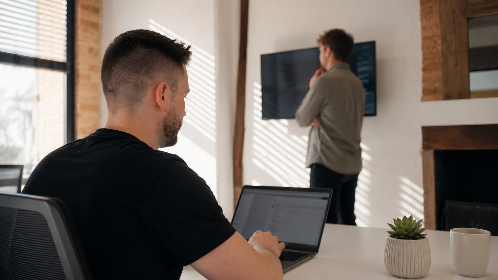 One of the team working at a laptop while a colleague studies code on a wall-mounted screen
