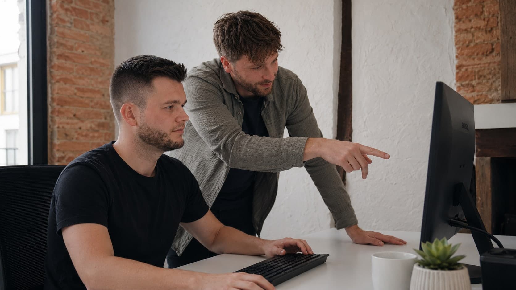 A colleague leaning in to point at something on a monitor while another works at the keyboard