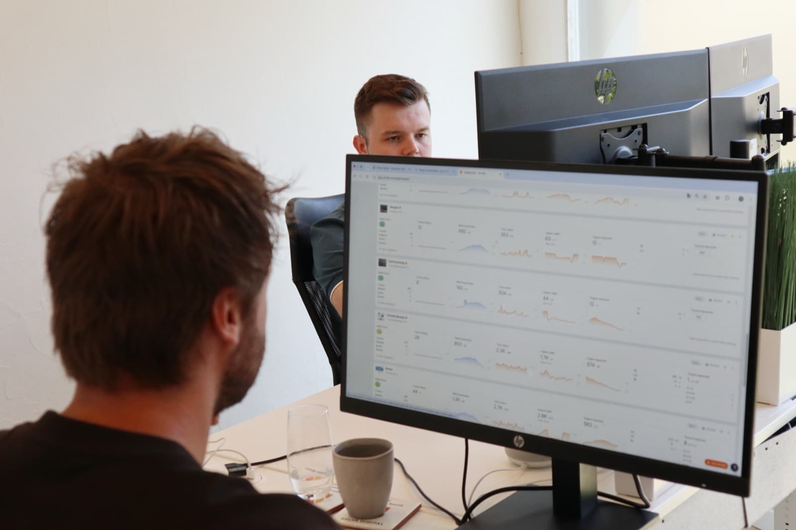 Vincent checking a client's analytics on his monitor, with Noah at the desk behind him