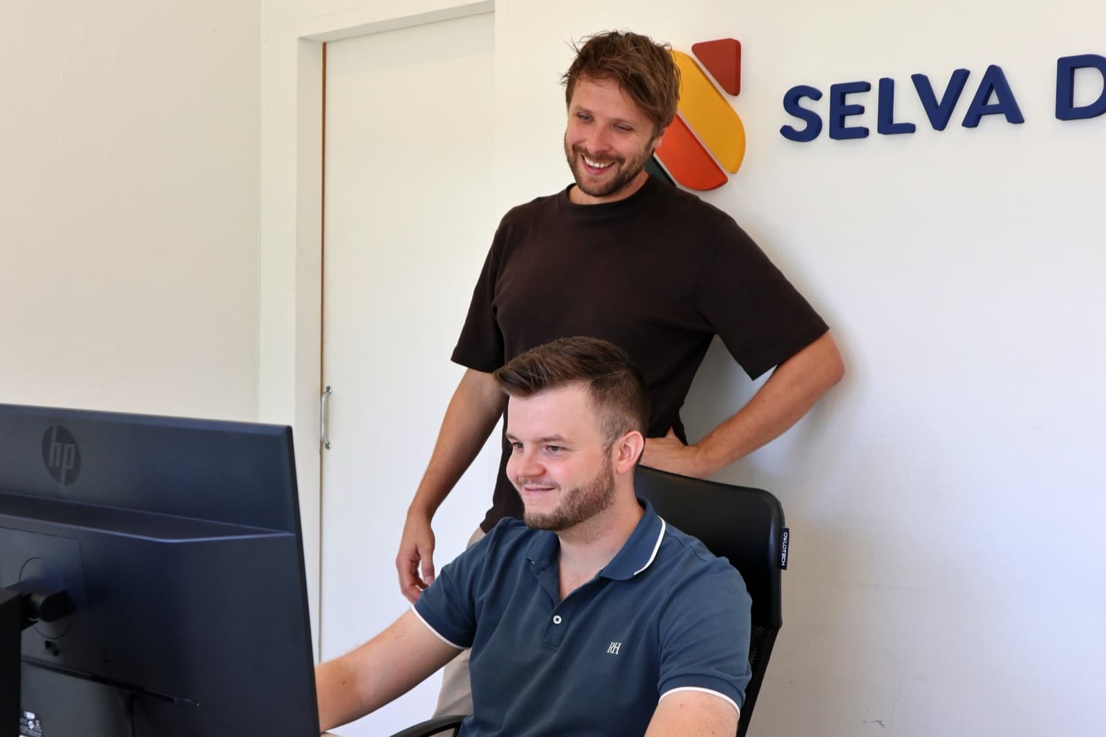 Vincent looking over Noah's shoulder at a client's site in the Selva Digital office